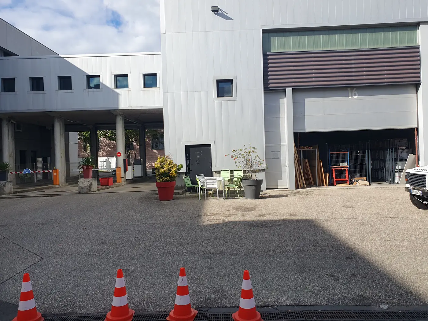 Avant travaux : une bande d'enrobé nue devant un bâtiment d'activité, balisée par des cônes de chantier.